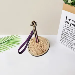 Portable wooden wrist yarn holder with purple strap and beige yarn ball on white table.