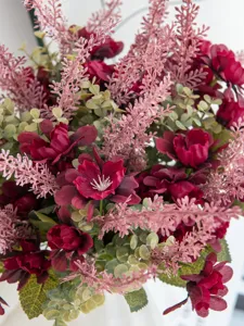 Nahaufnahme Detail des künstlichen Blumenstraußes mit roten Blüten und pinkem Laub, Deko.