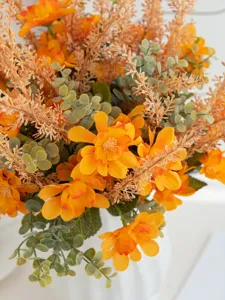 Künstlicher Blumenstrauß Detail, lebendige orangefarbene Gänseblümchen und Eukalyptus.