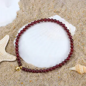 Close-up of natural red garnet beaded anklet on white seashell and sand background