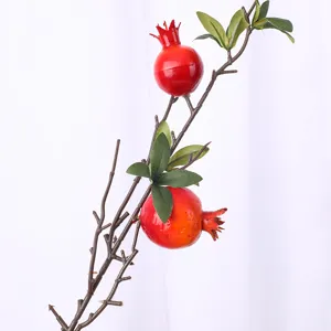Decorazione realistica con ramo di melograno artificiale con frutti rossi e foglie verdi.
