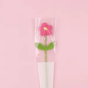 Handcrafted pink crochet puff flower shown inside a 'LOVE' themed gift packaging sleeve