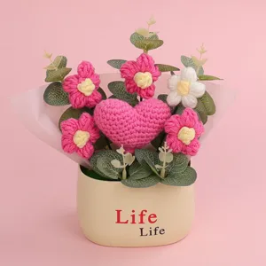 Detail view of a hand-knitted heart and puff flower crochet potted plant on pink background.