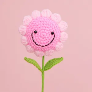 Detailed view of a hand-crocheted pink smiling flower with green stem and leaves.
