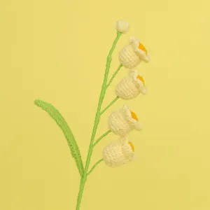 Macro view of delicate hand-knitted yellow crochet lily of the valley flowers and leaf