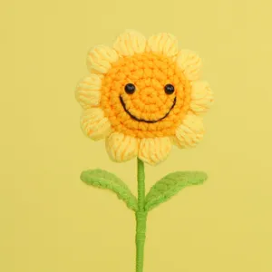 Close-up detail of a handmade crochet sunflower with a smiley face on yellow background