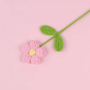 Macro detail of a handmade pink crochet puff flower featuring green leaves and a long stem
