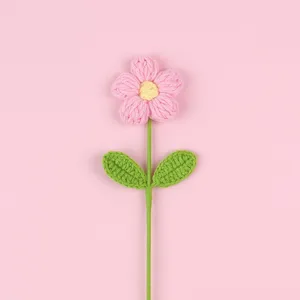 Detailed view of hand-crocheted pink puff flower with green leaves on pink background