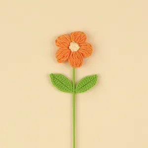 Close-up of handmade orange crochet puff flower with green leaves for home decor