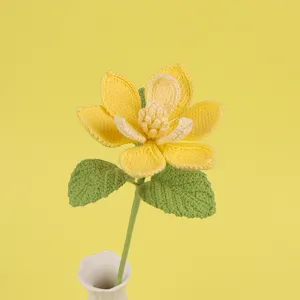 Close-up of a handmade yellow crocheted magnolia flower with green leaves in a white vase