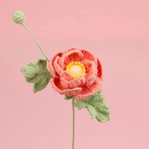 Handgemaakte gehaakte ranonkelbloem met koraalkleurige bloemblaadjes op roze achtergrond.
