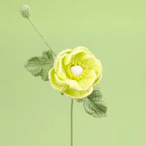 Macrodetail van een handgehaakte gele ranonkelbloem met groene bladeren en een knop.