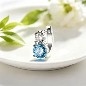 Close-up detail of stainless steel huggie earring with stacked clear and blue round stones