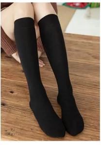 Close-up detail of women's black long knee-high socks displayed on rustic wooden floor surface.