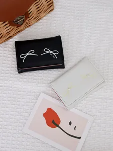 Close-up of trifold wallets with bow and pearl details in black and cream