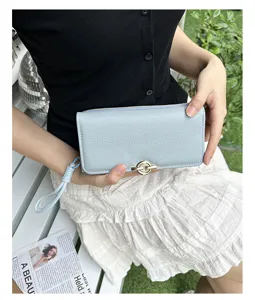 Vue détaillée d'un portefeuille long en cuir PU bleu clair à grain galet tenu par un modèle.