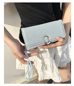 Close-up of light blue textured leather long wallet held by a model with a wrist strap.