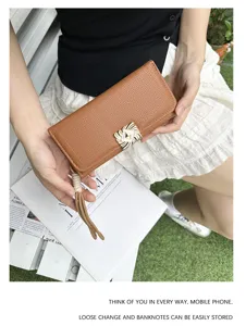 Handheld view of a brown pebbled leather long wallet with tassel and striped clasp