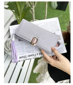 Detail view of a grey leather women's long wallet with a pink clasp held by a hand outdoors
