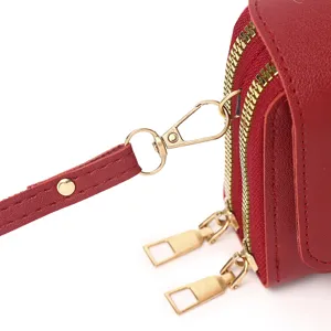 Detail shot of red leather phone bag with gold double zippers and strap clasp.
