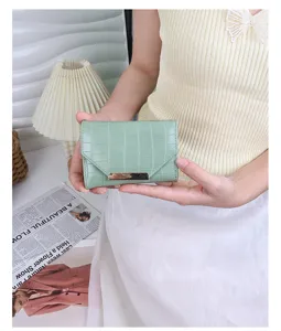 Détail d'un portefeuille à trois volets vert menthe motif crocodile tenu par un mannequin