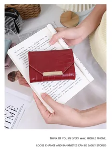 Gros plan d'un portefeuille à trois volets rouge foncé à motif crocodile tenu sur un livre