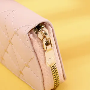 Close-up detail of smooth golden zipper on a light pink quilted leather women's wallet