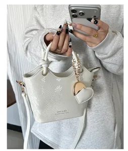 Primo piano di una borsa a secchiello bianca con trama a serpente e ciondolo a cuore oro.