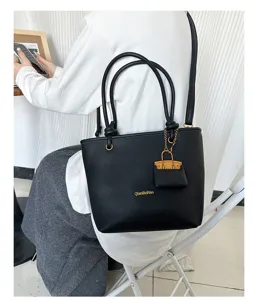 Black lychee grain tote bag shown worn on shoulder with stylish bag charm detail