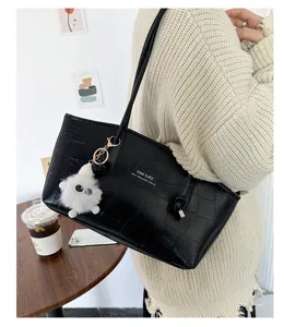 Close-up of a stylish black crocodile pattern tote bag with a white fluffy charm.