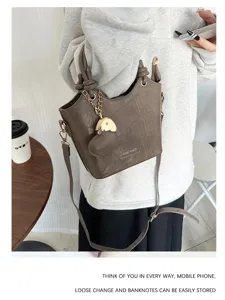 Elegante borsa a secchiello marrone coccodrillo con ciondolo a cuore portata a mano.
