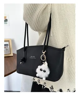 Close-up of black pebbled PU tote bag with a white fuzzy monster keychain