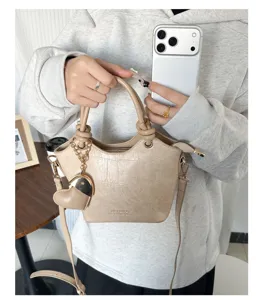 Dettaglio di una borsa a secchiello beige effetto coccodrillo con ciondolo a cuore e tracolla.