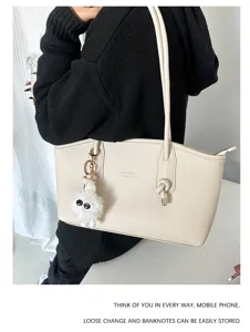 Detail view of a beige PU leather tote bag with a fluffy monster pendant and long straps