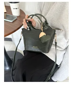 Dettaglio di una borsa a secchiello verde scuro motivo coccodrillo con ciondolo a cuore.