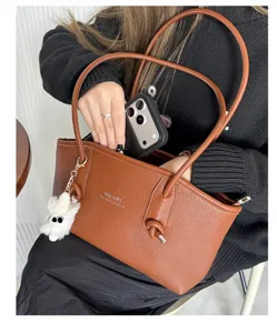 Close-up of brown PU leather underarm bag featuring a fluffy charm and pebbled texture
