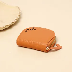 Detailed close-up of orange cat coin purse with cute embroidered face and leather texture.