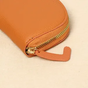 Detail of smooth metal zipper and litchi texture on orange leather wallet.