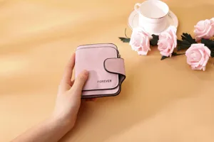Detail shot of a hand holding a pink matte PU leather wallet with FOREVER embossing.