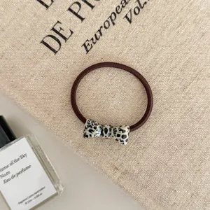 Close-up of a stylish leopard print bow hair tie presented on a beige fabric background.