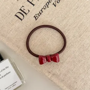 Detailed close-up showing the shiny red bow and elastic band on a textured beige fabric bag