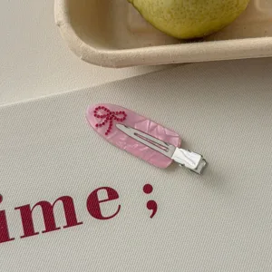 Close-up detail of a pink acrylic hair clip featuring a sparkling red rhinestone bow