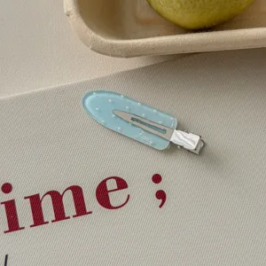 Close-up of a light blue glitter hair clip with white heart patterns and Fancy text