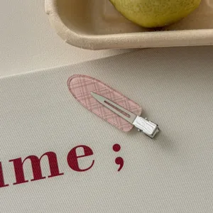 Close-up of a pink plaid pattern duckbill hair clip on a textured surface