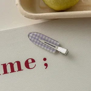 Detailed macro view of a purple gingham pattern duckbill hair clip on a textured background.