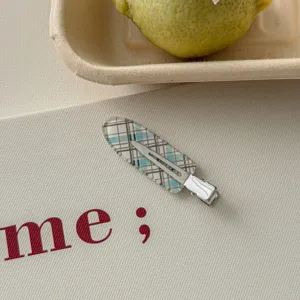 Detail shot of a blue and brown plaid pattern duckbill hair clip on a cream background.