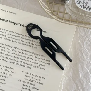 Detail view of a black acetate U-shaped hair fork shown on an elegant recipe background