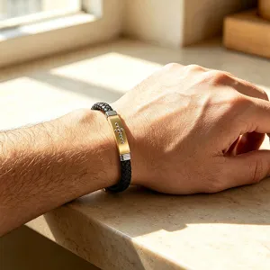Dettaglio di un bracciale in pelle intrecciata nera con piastra in acciaio dorata e croce.