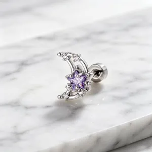 Close-up of a silver moon and purple zircon star stud earring on white marble surface.