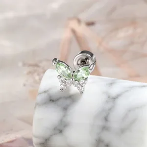 Detailed close-up of a butterfly-shaped titanium stud with green and clear stones.